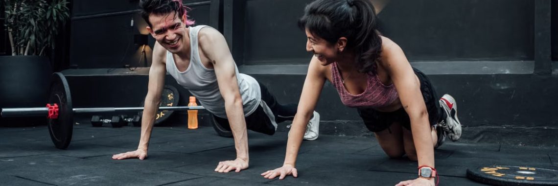 Man and woman doing pushups while smiling during a workout inside a Mexico City gym.